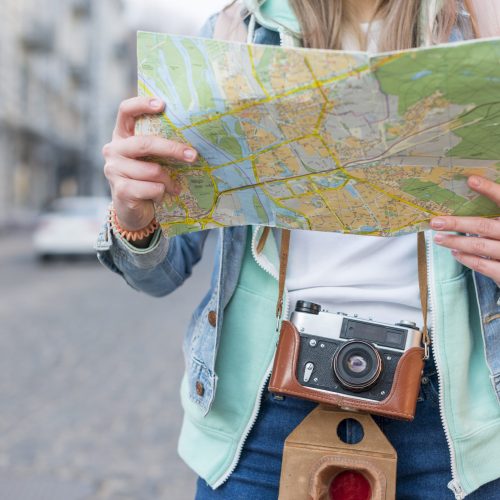 mid-section-female-traveler-with-camera-holding-map-hand